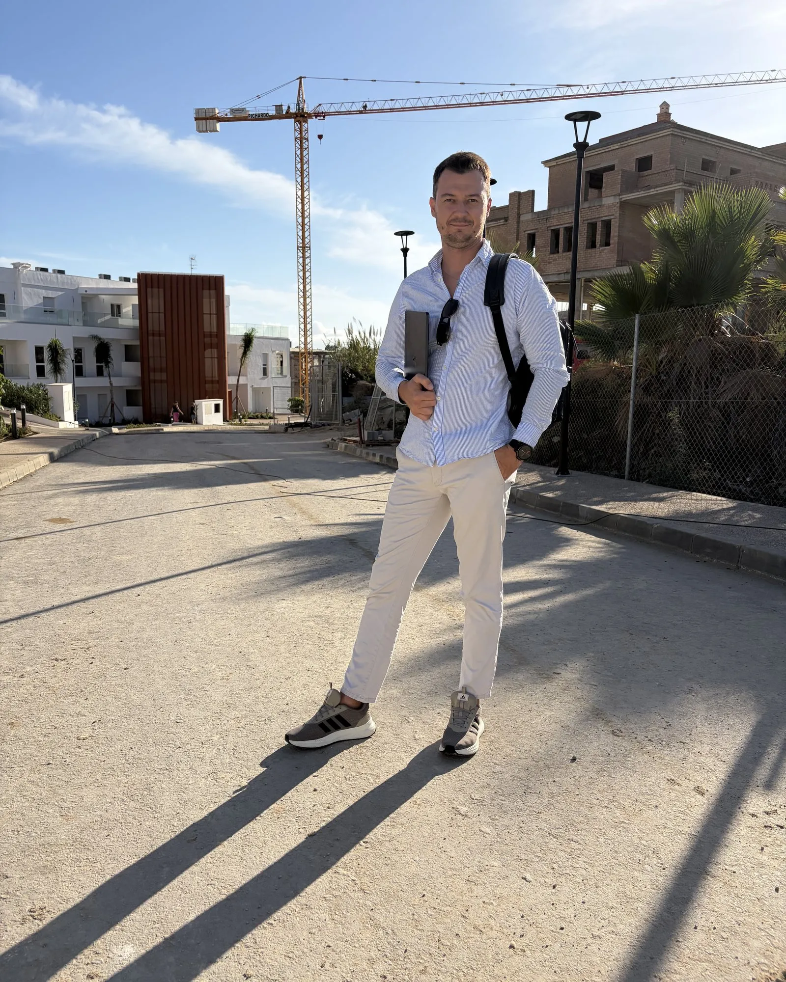 Oleg Chupryna standing on a road in a new-build development, with a tower crane and homes under construction behind him