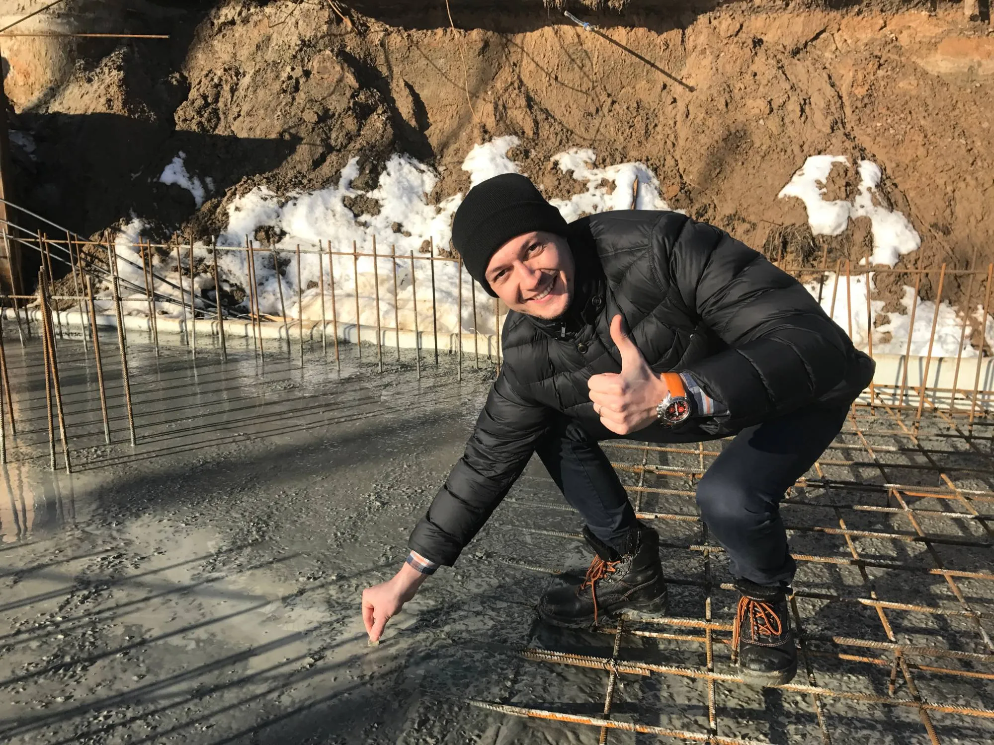 Oleg Chupryna crouching on a building site during a concrete pour, among the steel reinforcement, giving a thumbs up